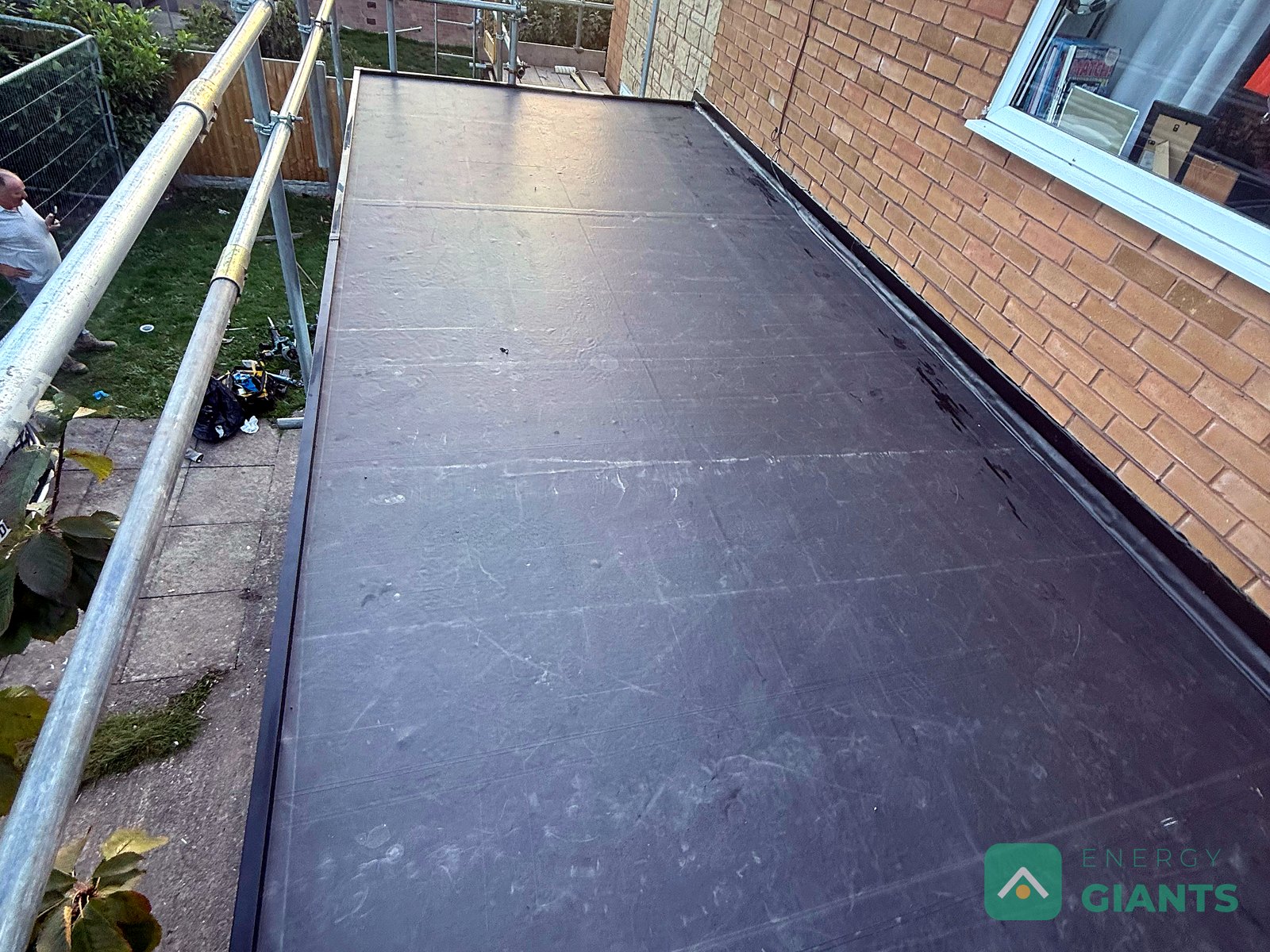 The finished EPDM membrane on the garage roof in Ruthin, seen from the scaffold, with the neighbouring garden beyond