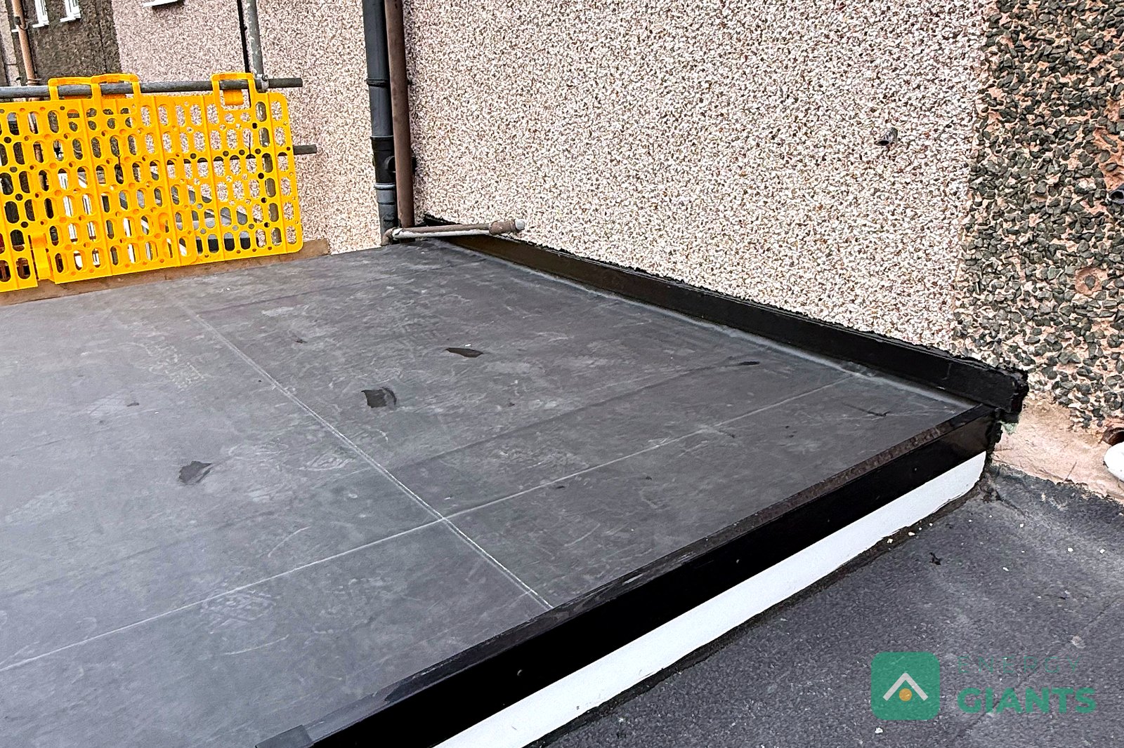 The finished EPDM warm roof over a rear extension, with new white edge trims and the rendered house wall behind