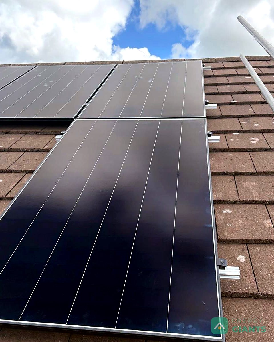 Black Aiko panels on the concrete tiled roof, photographed from the scaffold, with bird mesh fitted along the edge