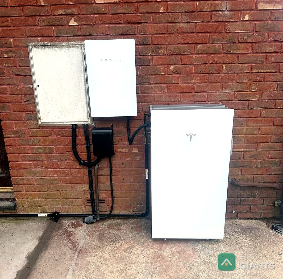 Tesla Powerwall 3 mounted on the outside brick wall of the house beside its isolator enclosure