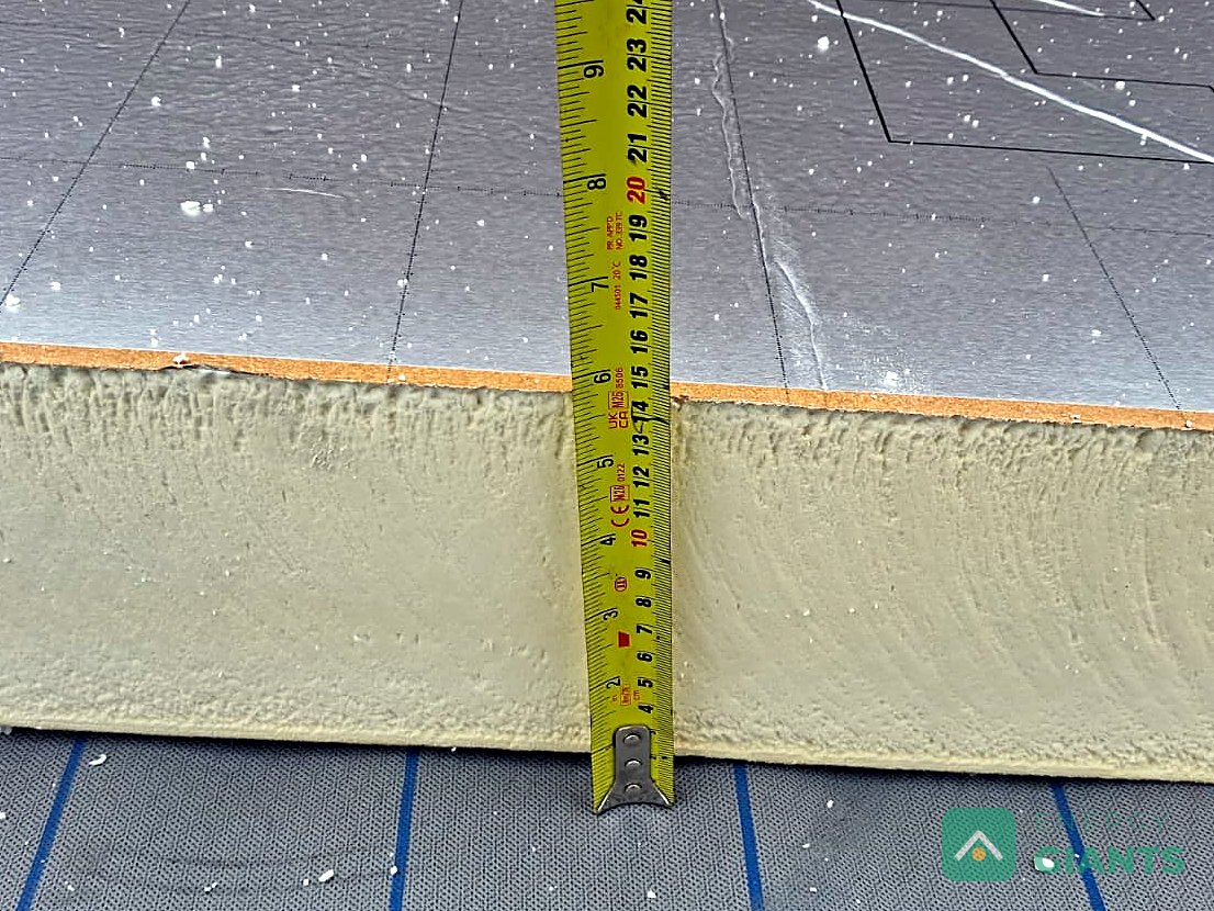 A tape measure held against the edge of a foil faced PIR insulation board on the roof, reading over 100 millimetres