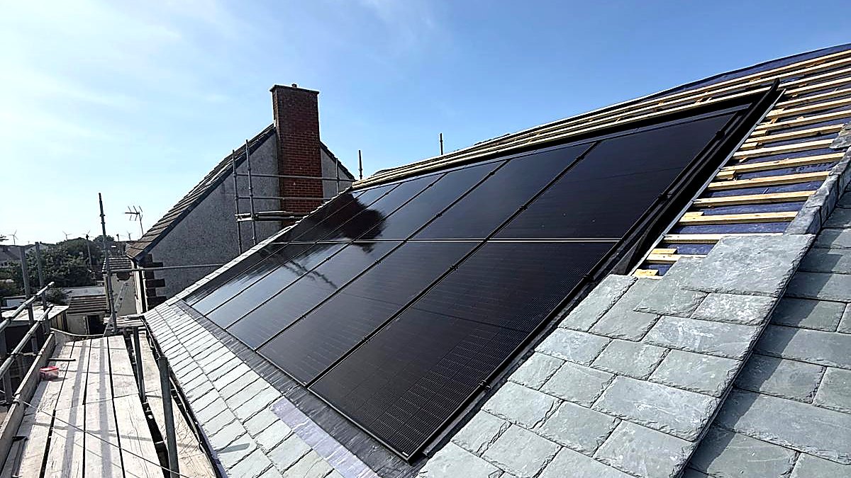Black solar panels set flush into a new green grey slate roof, with battens still open on the next plane and a blue sky behind