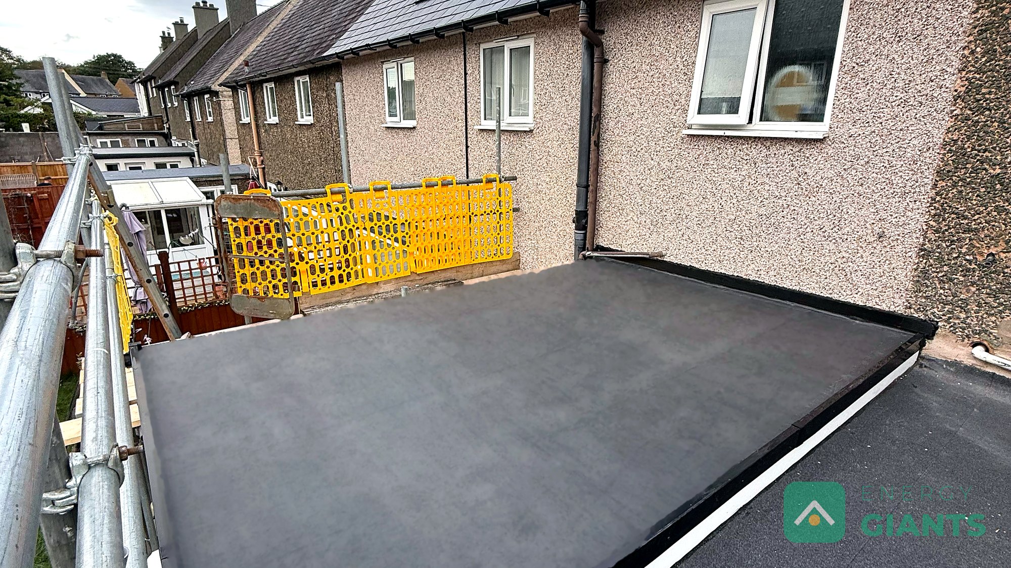 The finished black EPDM warm roof over a rear extension in Llanrwst, seen from the scaffold, with the rendered back wall of the house behind