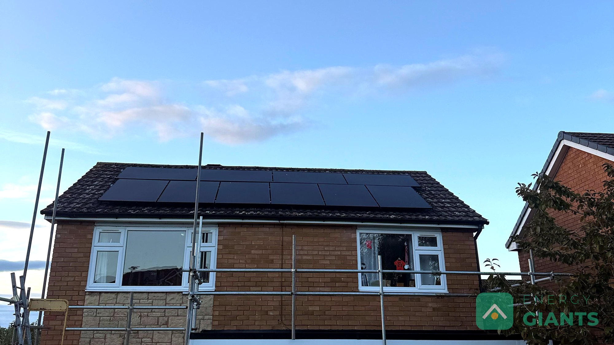 A brick semi detached house in Ruthin from the road, the garage flat roof newly finished in black EPDM with white fascias, scaffold still up