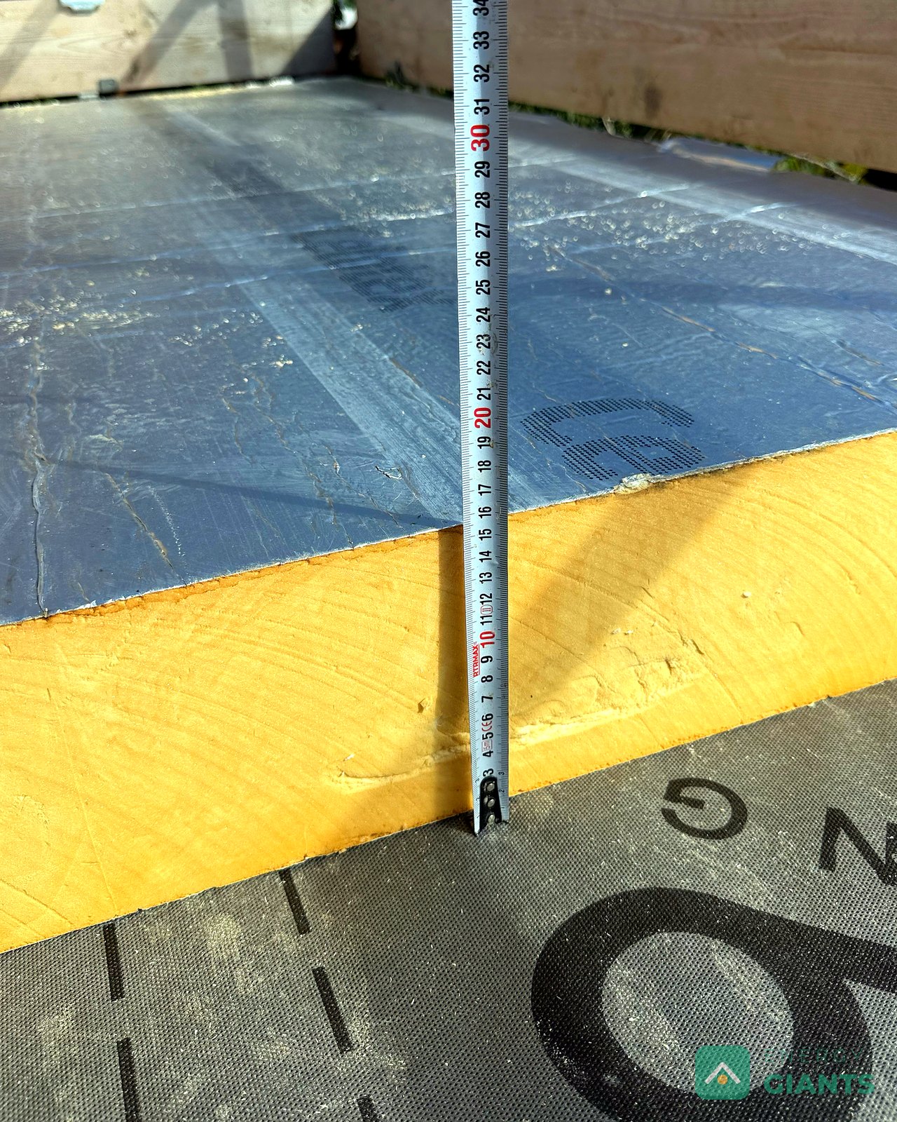 A tape measure held against the edge of a foil faced PIR insulation board on the roof, reading over 100 millimetres