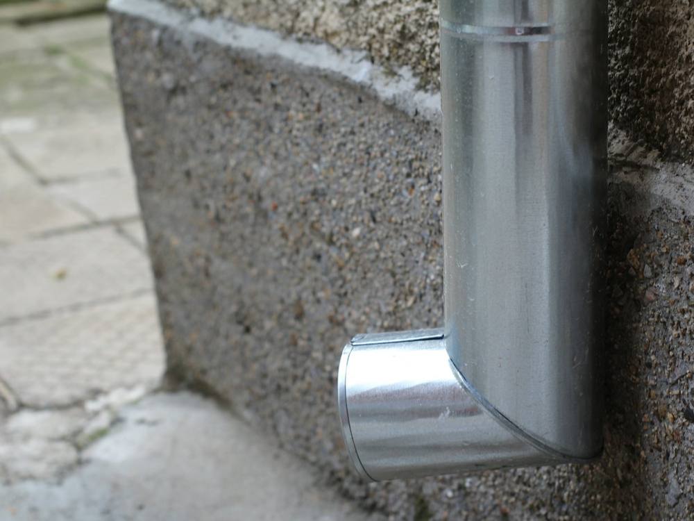 An aluminium downpipe ending in a shoe above a paved path