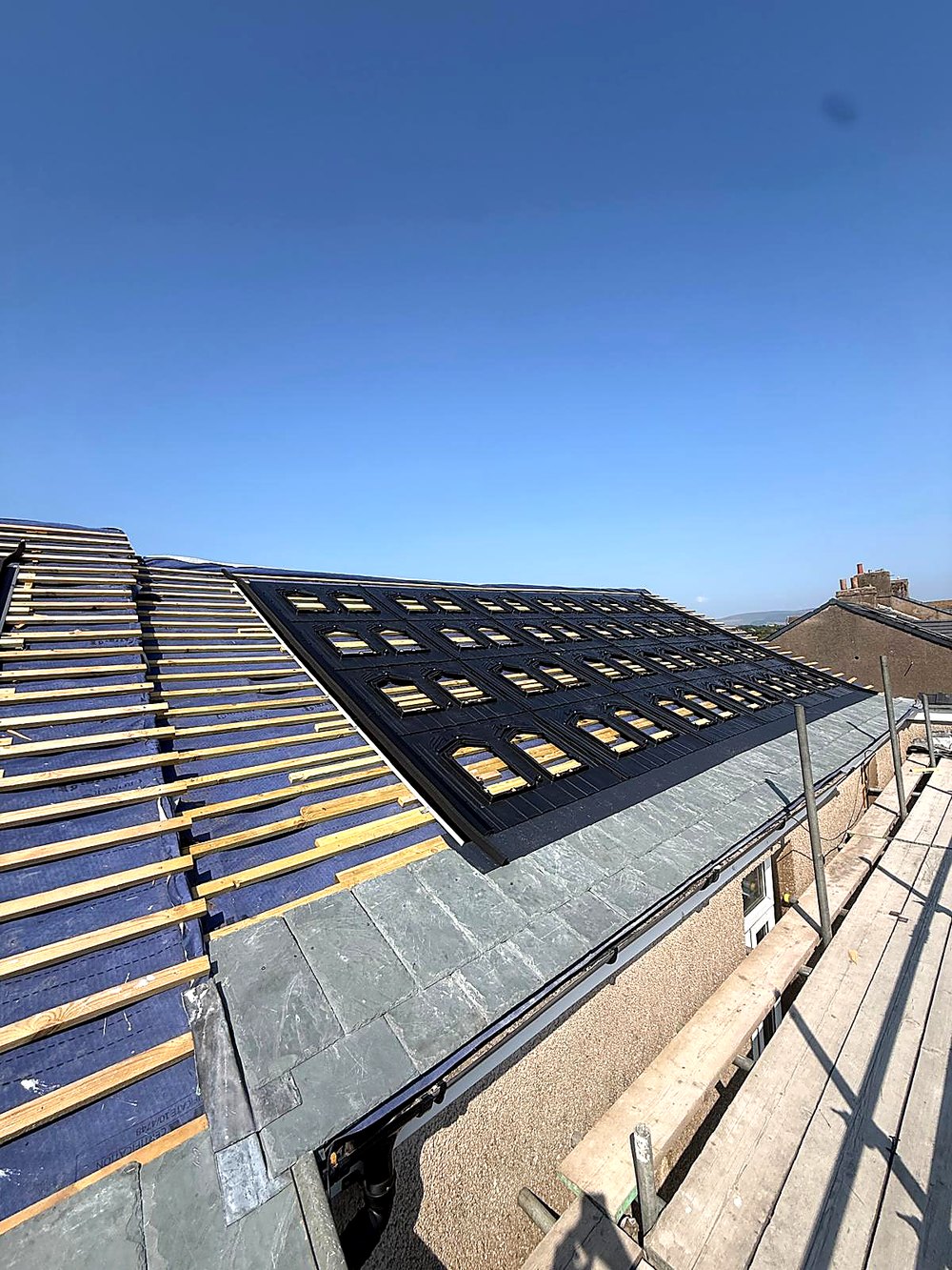 The roof plane half finished: membrane and battens exposed on the left, mounting trays and new slate on the right