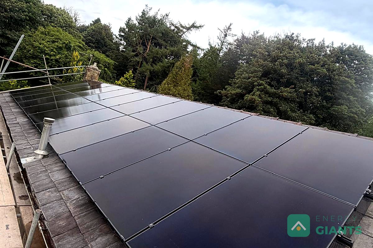 Twenty two black Aiko panels along a natural slate roof with a stone chimney and mature trees behind, in Great Harwood