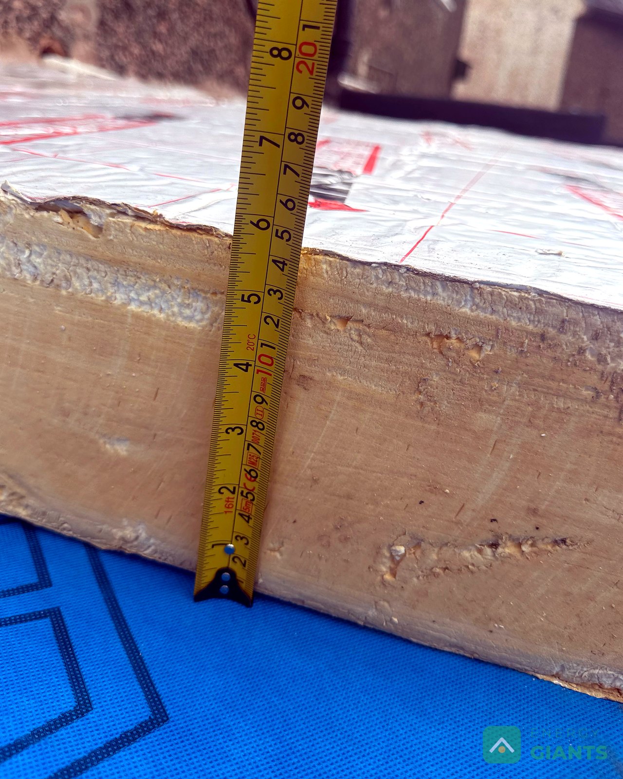 A tape measure held against the edge of a foil faced PIR insulation board on the roof, reading over 100 millimetres