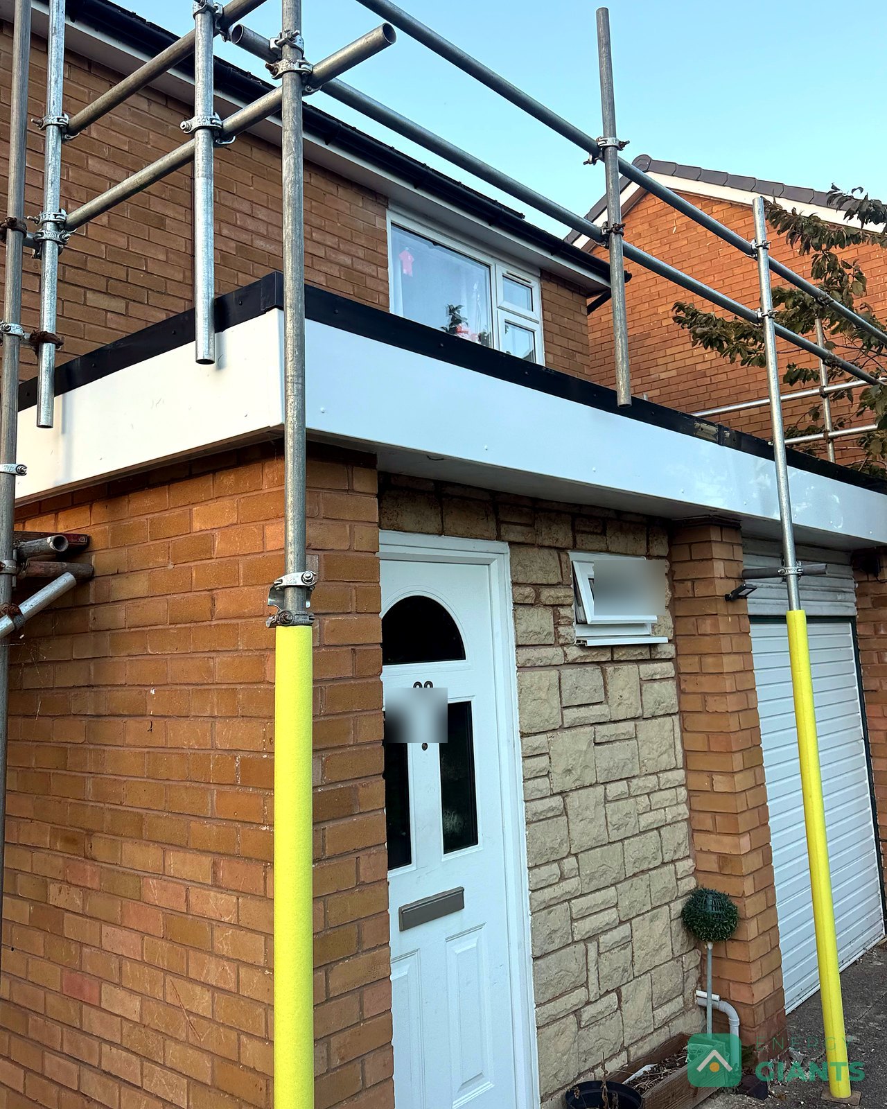 New white fascia boards and a black drip edge on the front of the garage roof, seen from below the scaffold
